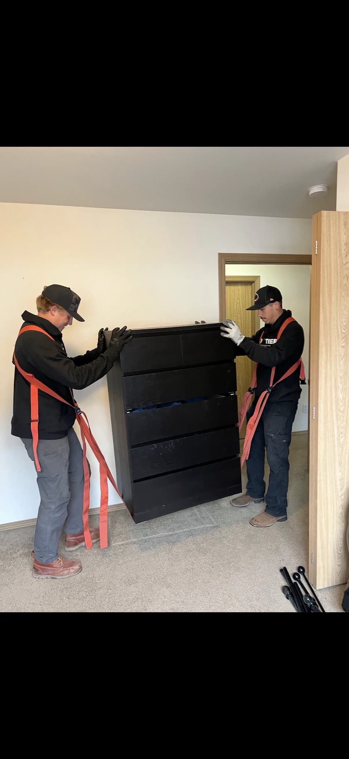 Two Top Tier crew members carrying a dresser with moving straps